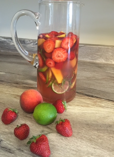 Large jug of strawberry peach sangria alongside some fruit.