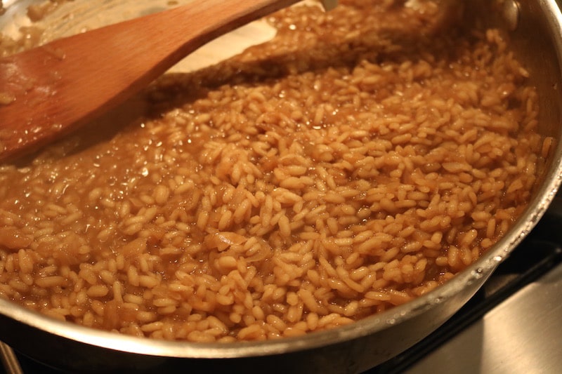 Homemade risotto in a pan being stirred by a wooden spoon.