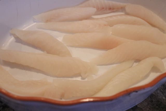 Strips of raw tilapia in a a white casserole dish.