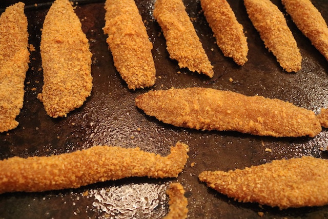 Breaded tilapia fish strips on a sheet pan after being baked in the oven.