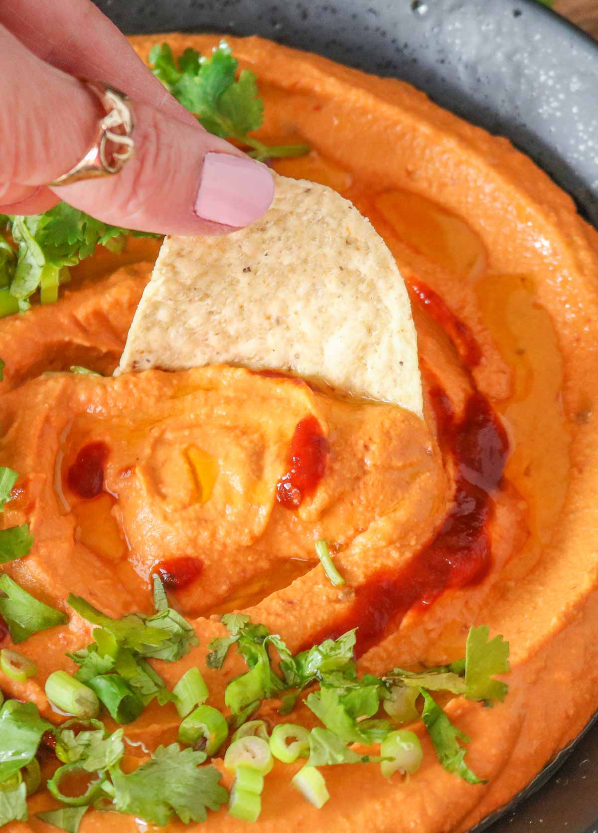 Hand holding a tortilla chip, dipping it into a bowl of hummus.