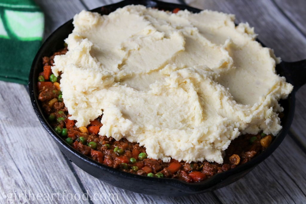 Skillet of shepherd's pie topped with creamy mashed potatoes before being baked.