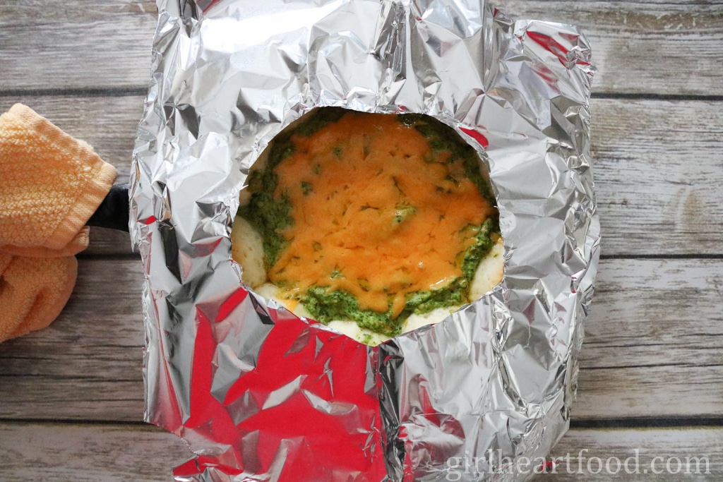 Cheesy spinach artichoke dip partially covered by aluminum foil.