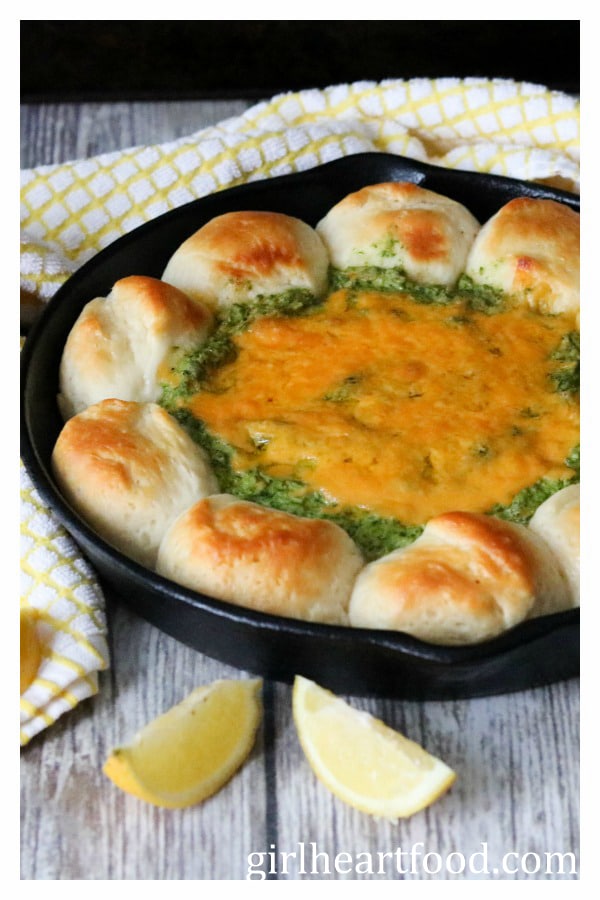 Spinach artichoke dip and biscuits in a skillet next to lemon and a tea towel.