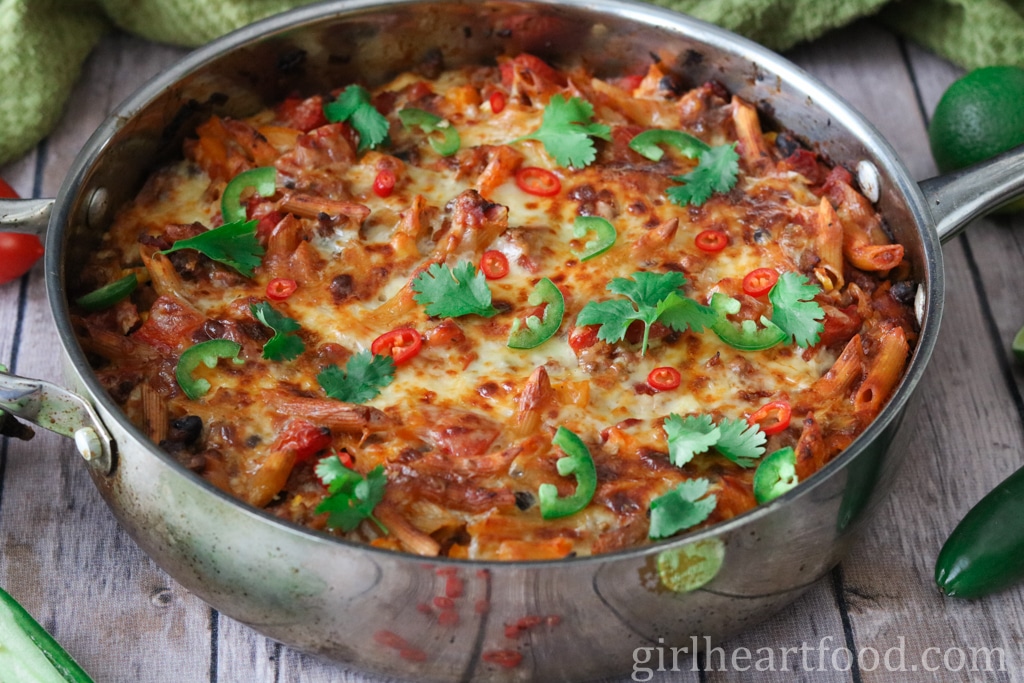 Cheesy pasta bake in a pan garnished with cilantro and sliced chili peppers.