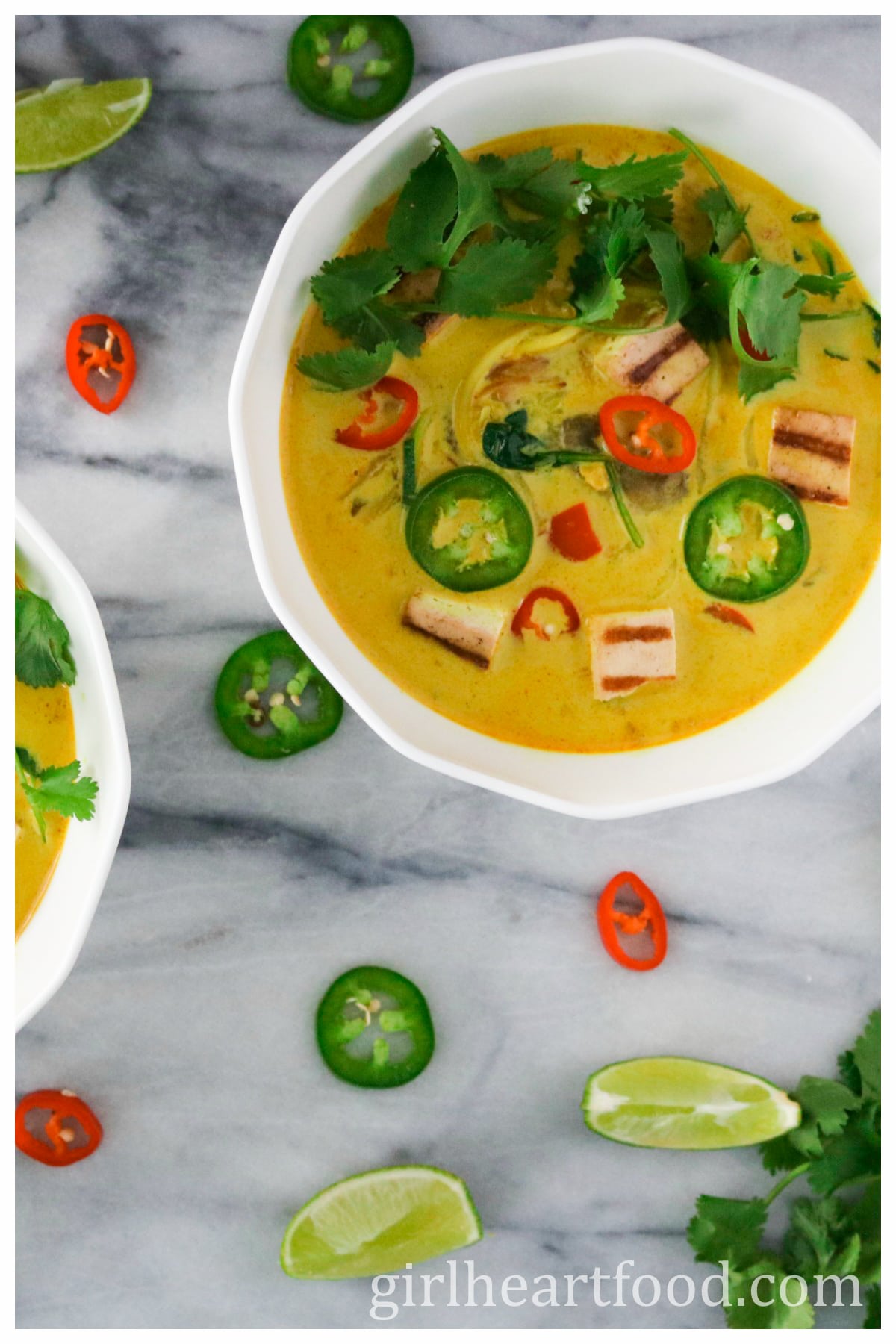 Bowl of tofu and vegetable curry coconut soup next to chili pepper, lime wedges & cilantro.