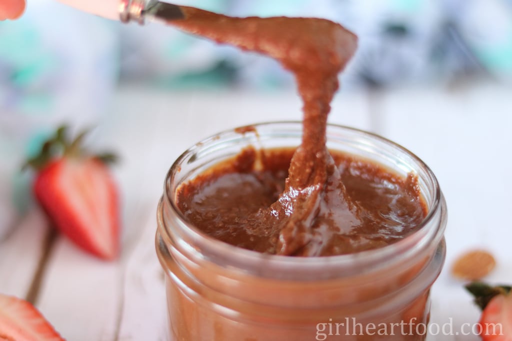 Spreader scooping up chocolate almond butter from a jar.