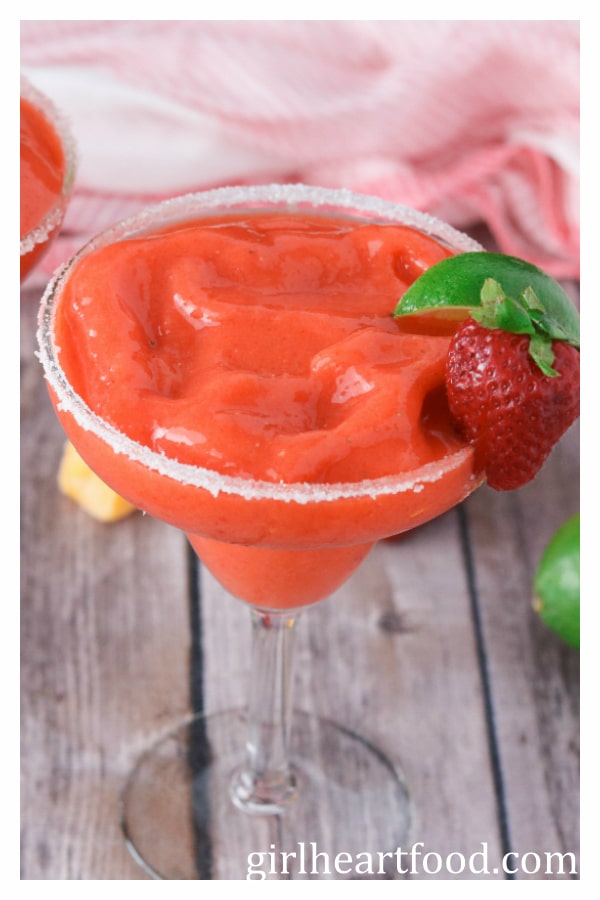 Glass of frozen strawberry mango margarita garnished with a strawberry and lime wedge.