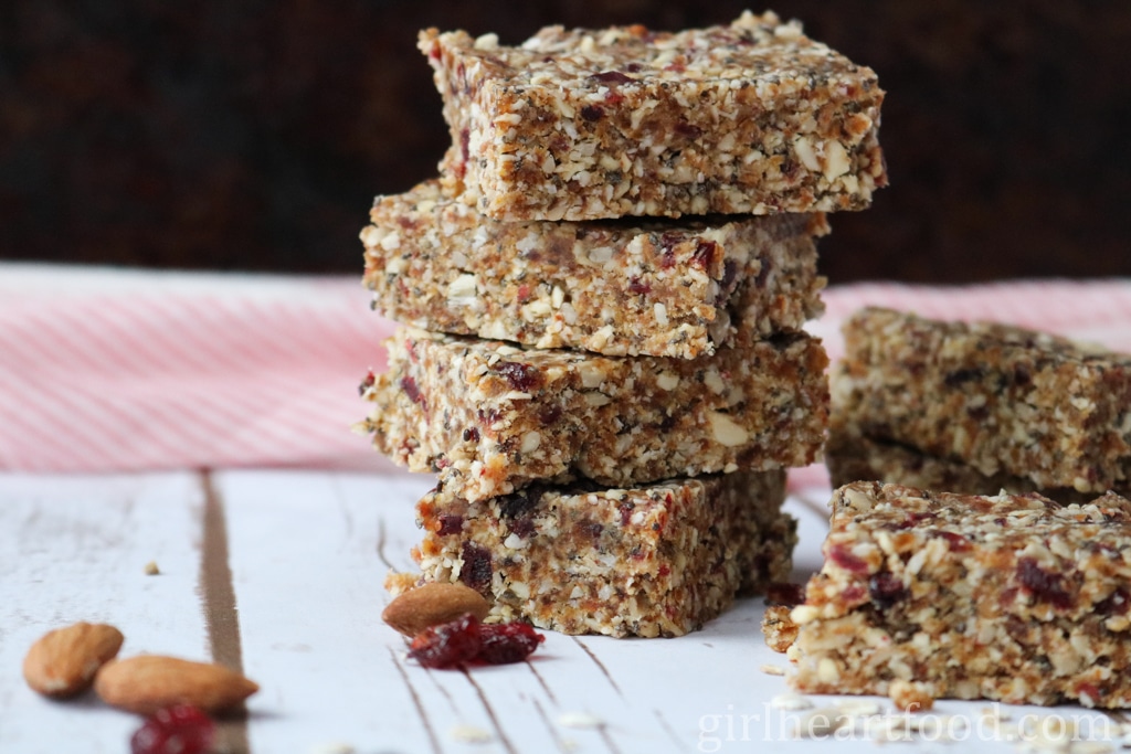 Stack of four granola bars next to almonds and cranberries and more granola bars.