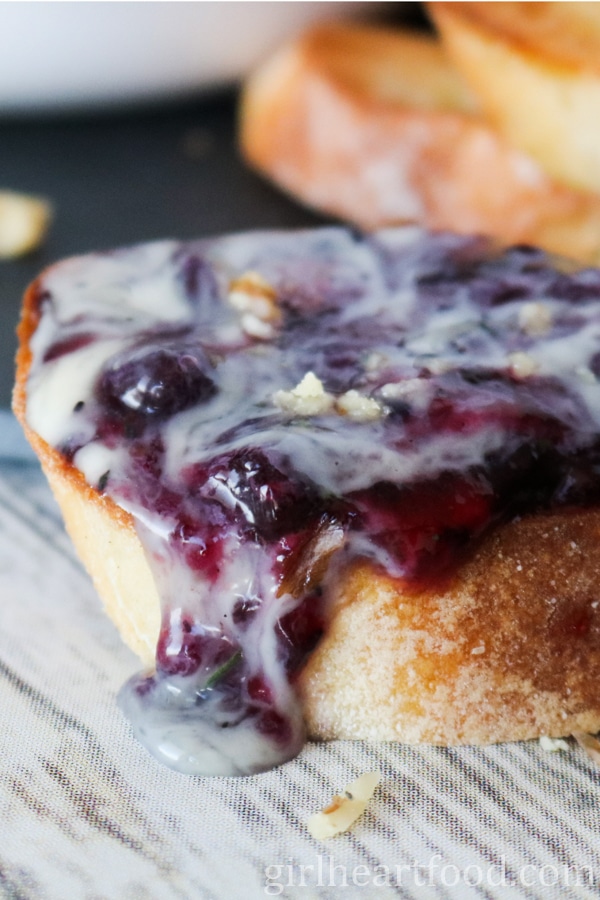 Close-up of a piece of bread with blueberry and melted camembert on top.
