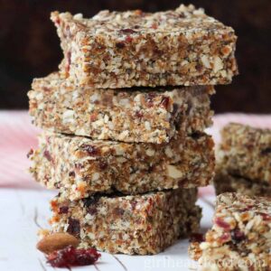 Stack of four no bake granola bars next to an almond and dried cranberry.