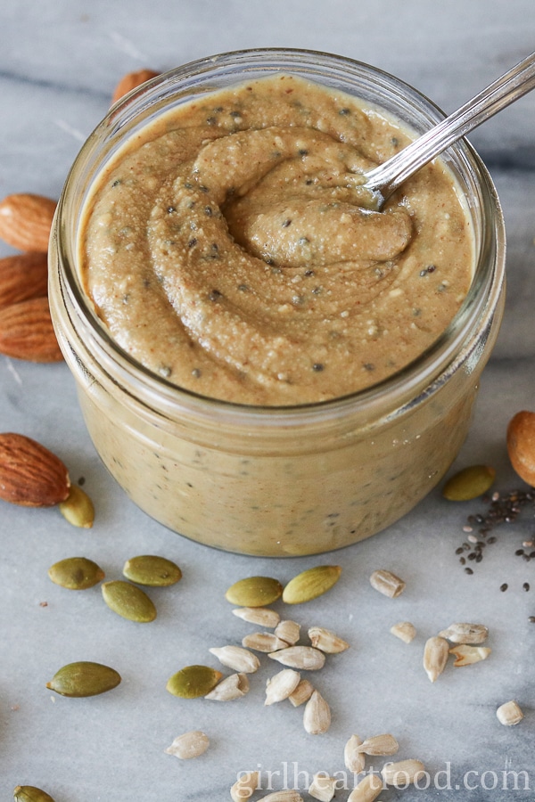 Jar of mixed nut and seed butter with a spoon dunked into the butter.