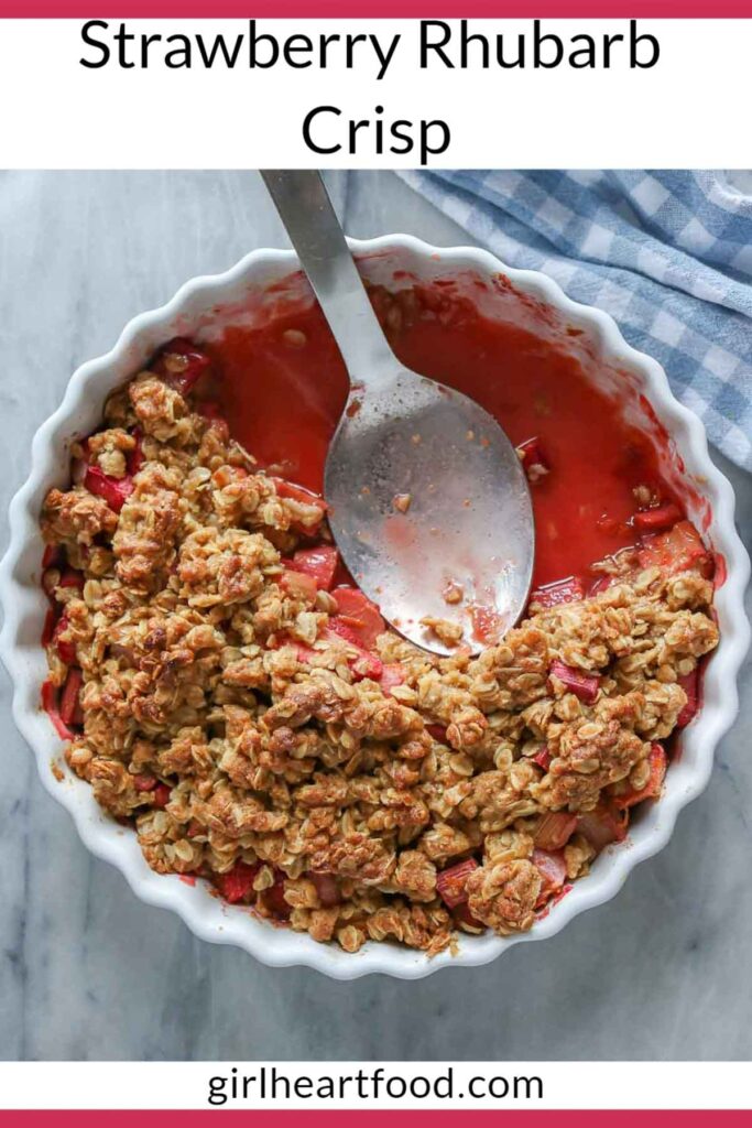 Partially eaten strawberry rhubarb crisp in a serving dish with a serving spoon resting in it.