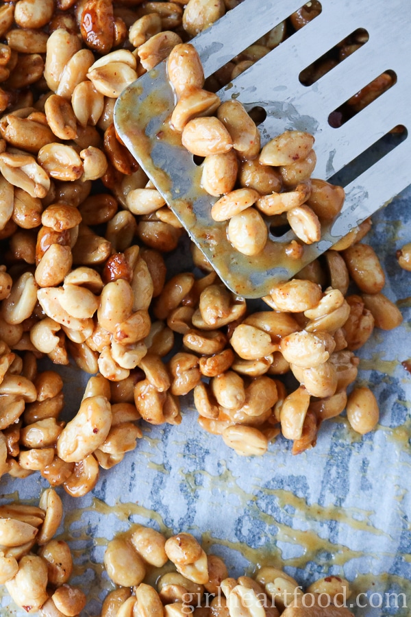 Spatula lifting nuts off a parchment paper-lined sheet pan.