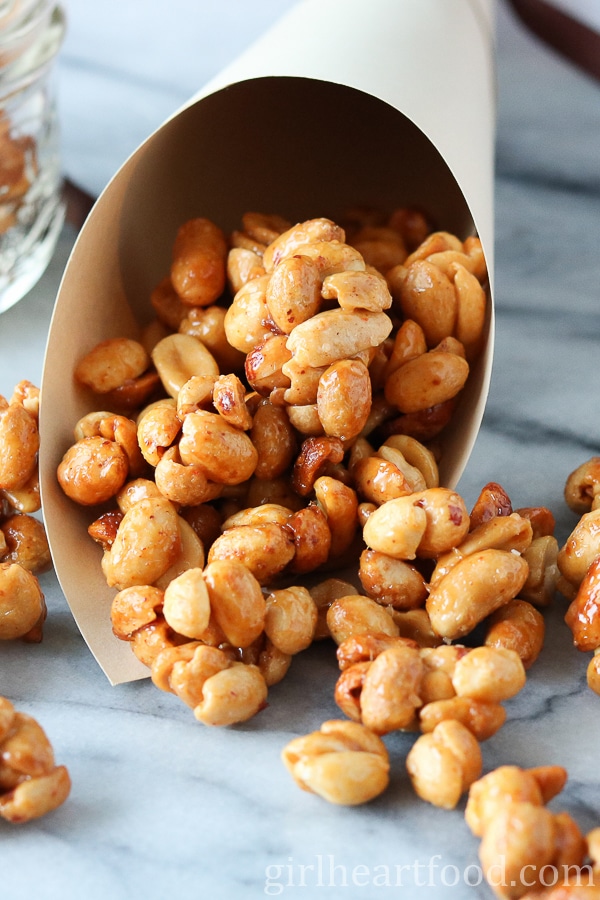 Honey roasted peanut clusters spilling out of a paper cone and onto a marble board.