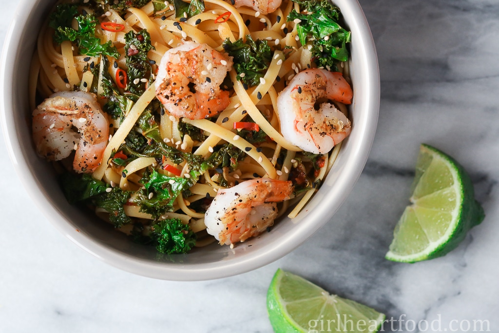 Bowl of chili shrimp pasta alongside lime wedges.