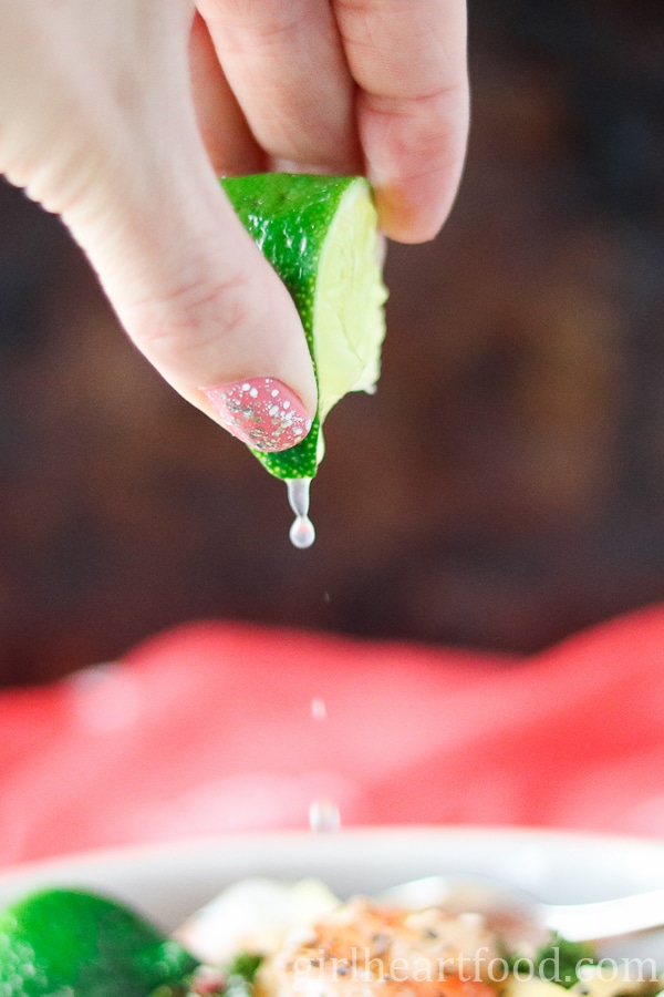 Hand squeezing lime over a bowl of food.