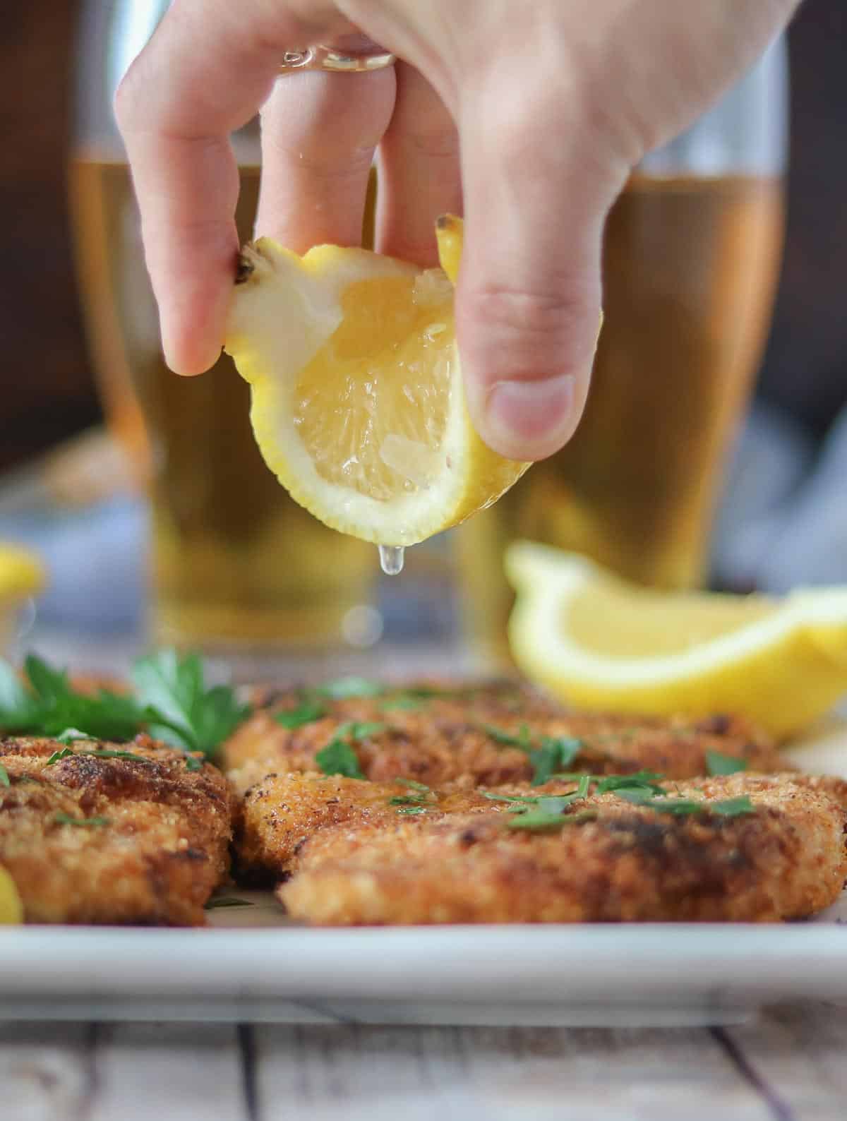 Hand squeezing a lemon wedge over pork schnitzel.