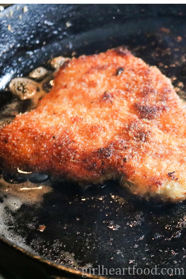 A piece of breaded pork schnitzel frying in a cast-iron pan.