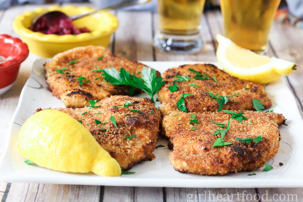 Four pieces of pork schnitzel on a plate garnished with parsley.