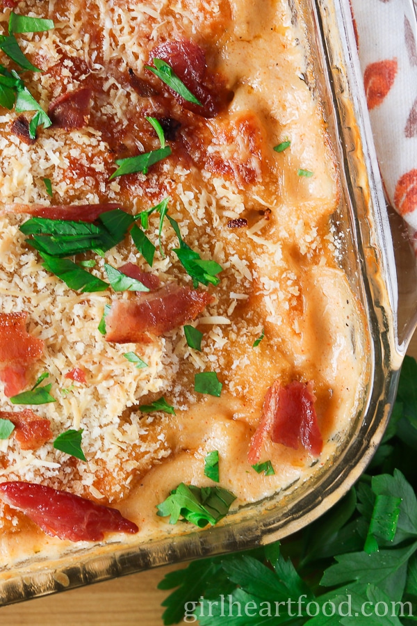 Close-up of mac and cheese in a baking dish garnished with crispy bacon and parsley.