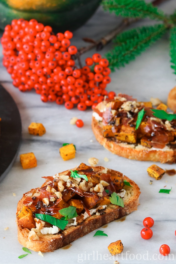 Roasted acorn squash crostini on a marble board next to dogberries.