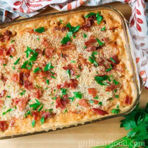 Baking dish of of creamy baked mac and cheese with parsley and crispy bacon pieces on top.
