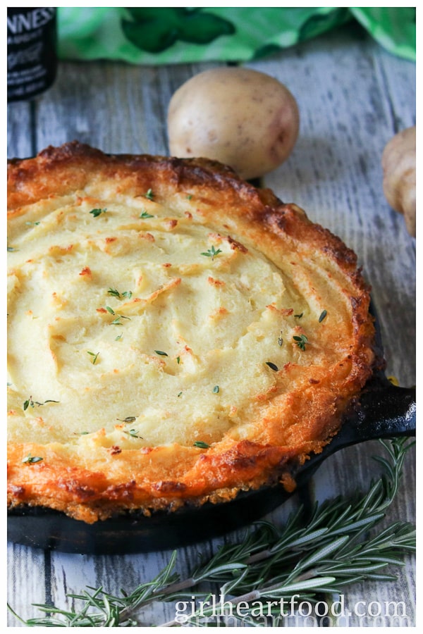 Skillet of shepherd's pie next to rosemary and potatoes.