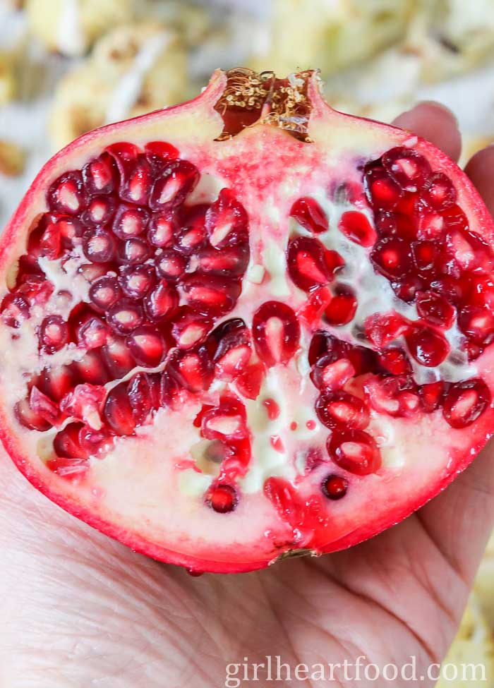 Hand holding half a pomegranate, showing the interior.