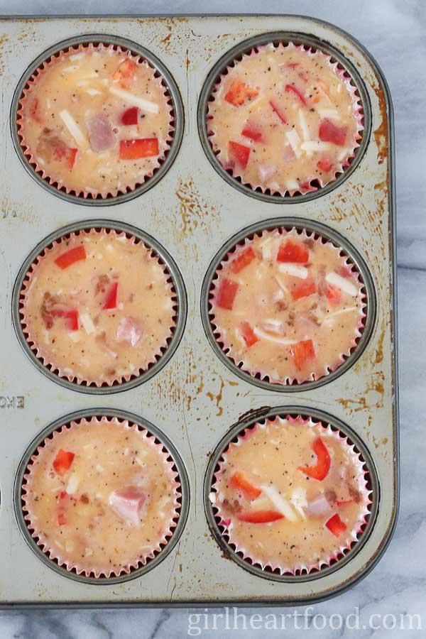 Ham and egg muffins in a muffin tin before being baked.