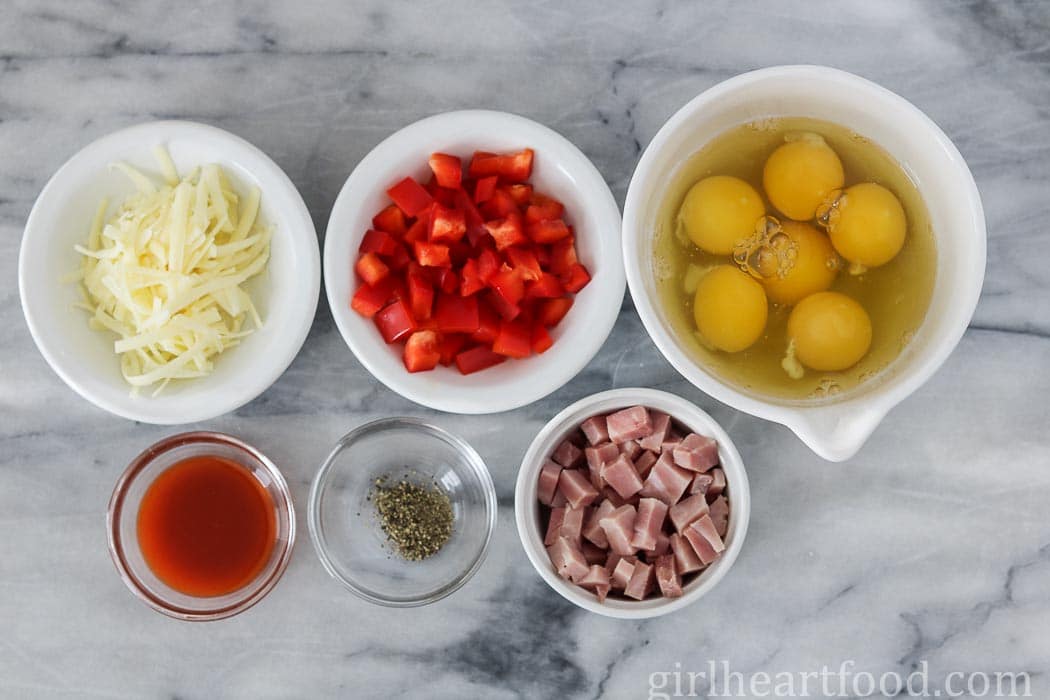 Ingredients for ham and egg muffins in dishes on a marble board.