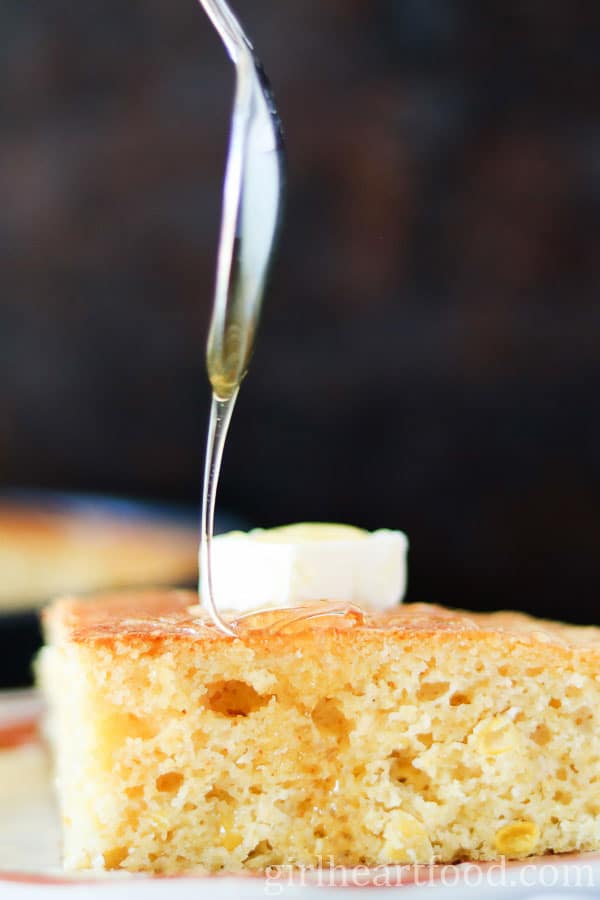 Spoon drizzling honey over a slice of cornbread.