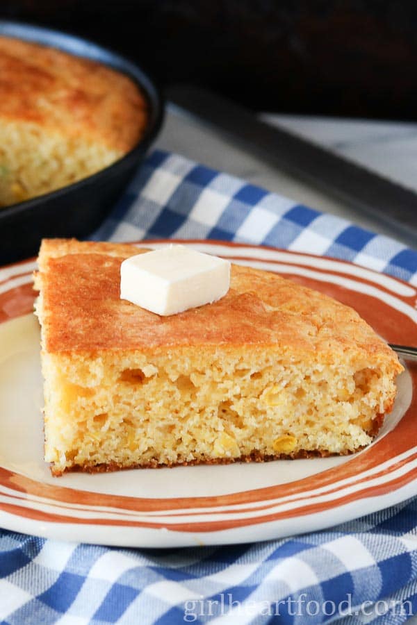 Slice of cornbread on a plate with a dab of butter over top.