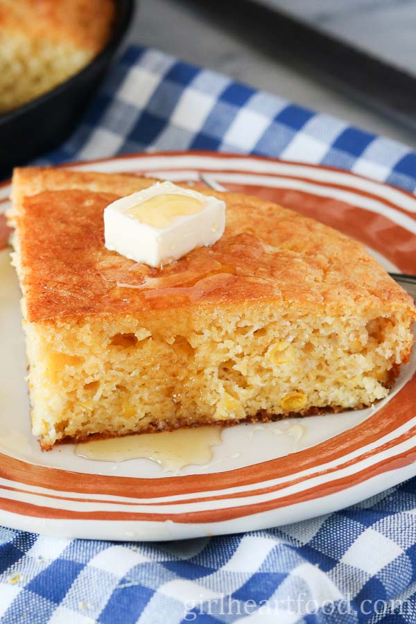 Slice of cornbread on a plate with a dab of butter and honey over top.