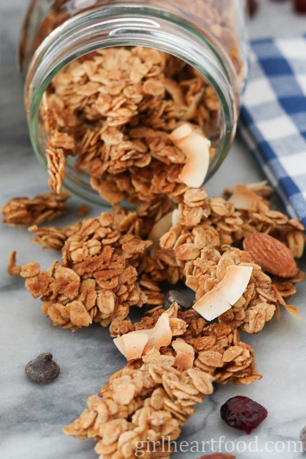 Crunchy homemade granola pouring out of a jar that's tipped on its side.