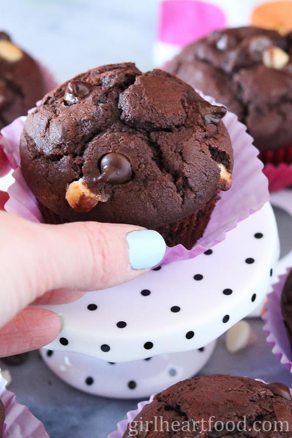 Hand reaching for a triple chocolate muffin on a polka dot stand.