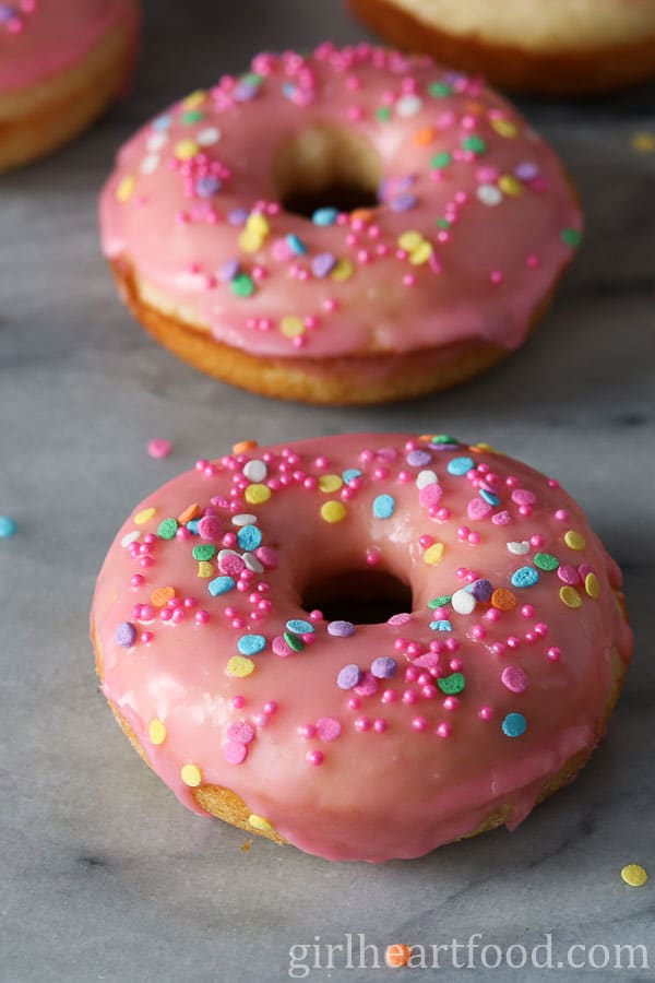 Pink vanilla glazed donuts with sprinkles on a marble board.