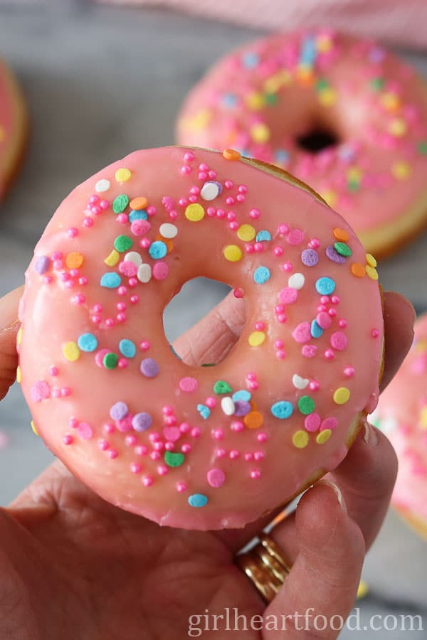 Hand holding a pink glazed donut with sprinkles.