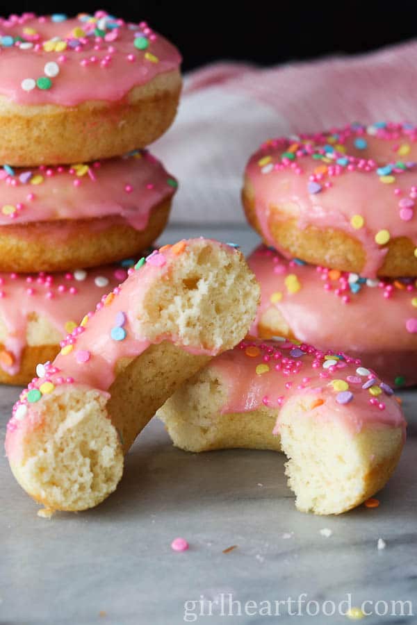 Two halves of a pink glazed donut with sprinkles, one half resting on the other.