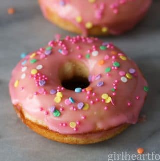 Pink glazed vanilla donut with sprinkles on a marble board.