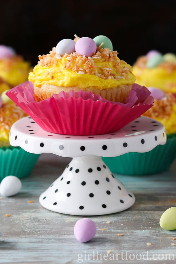 Vanilla cupcake garnished with coconut and candy, sitting on a stand.