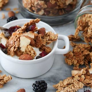 Homemade granola and yogurt in a white dish alongside some more granola spilling out of a jar.