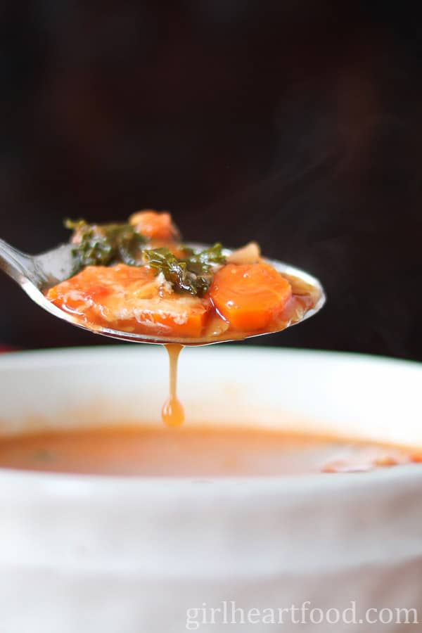 A steaming spoonful of soup with broth dripping into a bowl.