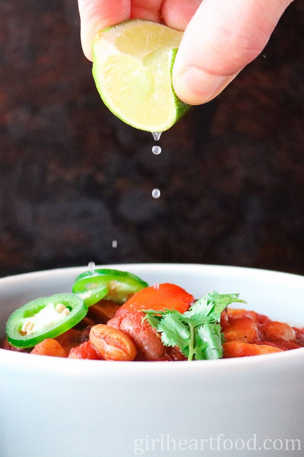 Hand squeezing a lime over a bowl of 3 bean chili.