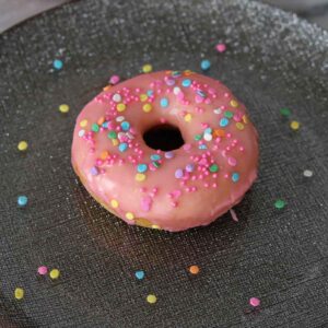 Pink glazed vanilla donut with sprinkles on a plate.