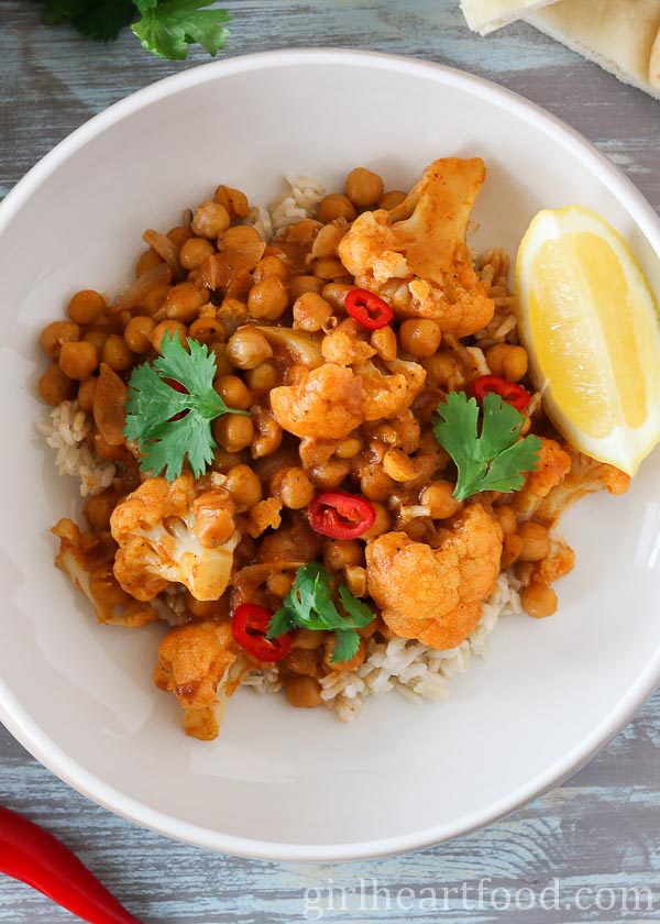 Overhead shot of a bowl of chickpea cauliflower curry and rice garnished with toppings.