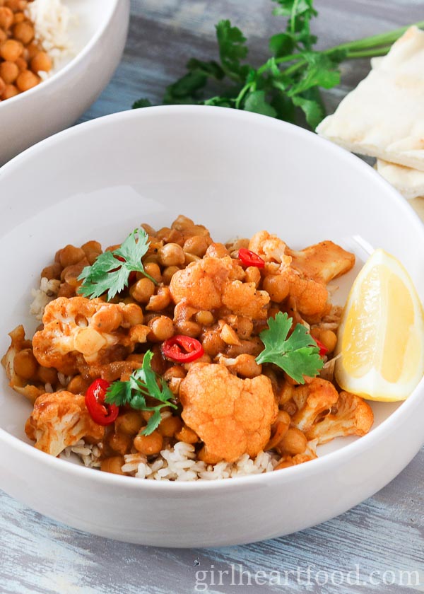 Bowl of chickpea cauliflower curry and rice garnished with chili pepper, cilantro and lemon.