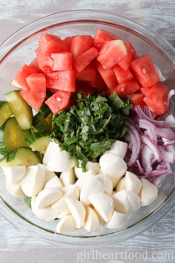 Ingredients for cucumber melon salad with bocconcini in a bowl before being mixed together.