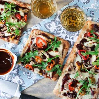 BBQ chicken flatbread pizza next to wine, BBQ sauce and hot peppers.
