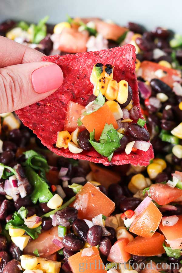 Hand holding a tortilla chip with chunky black bean and corn salsa.